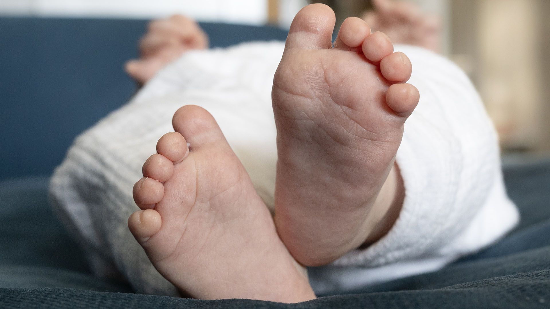 Gros plan des pieds nus d'un bébé, enveloppés dans une couverture blanche, sur un fond bleu doux.