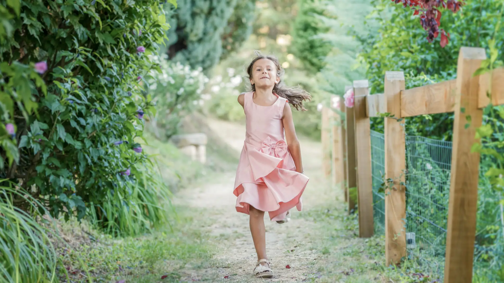 Gros plan d'une jeune fille aux cheveux châtains clairs tressés, vêtue d'une robe bleu foncé, regardant directement l'appareil photo tout en tenant les cordes d'une balançoire, avec un arrière-plan flou et doré.