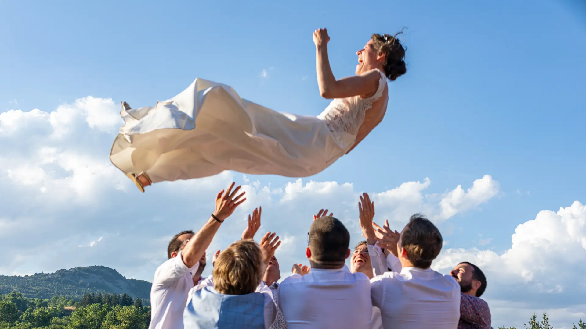 Photo en noir et blanc d'un couple de mariés debout sur un balcon au-dessus d'une foule d'invités. La mariée tient un bouquet de fleurs et le marié la regarde. Les invités en dessous regardent vers le haut, certains souriant et agitant des éventails.