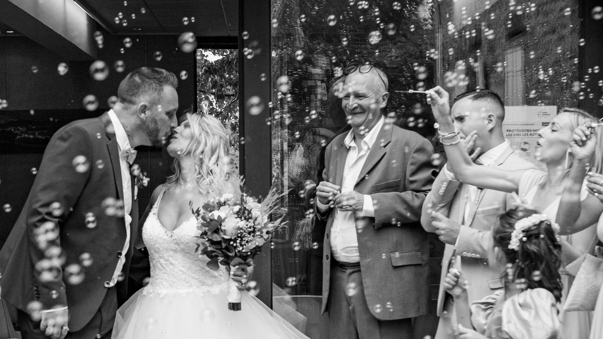 Gros plan d'une mariée tenant un bouquet de mariage coloré composé de roses roses et blanches, de chrysanthèmes blancs et de diverses petites fleurs violettes et verdoyantes. La mariée est légèrement floue en arrière-plan, montrant sa robe blanche.