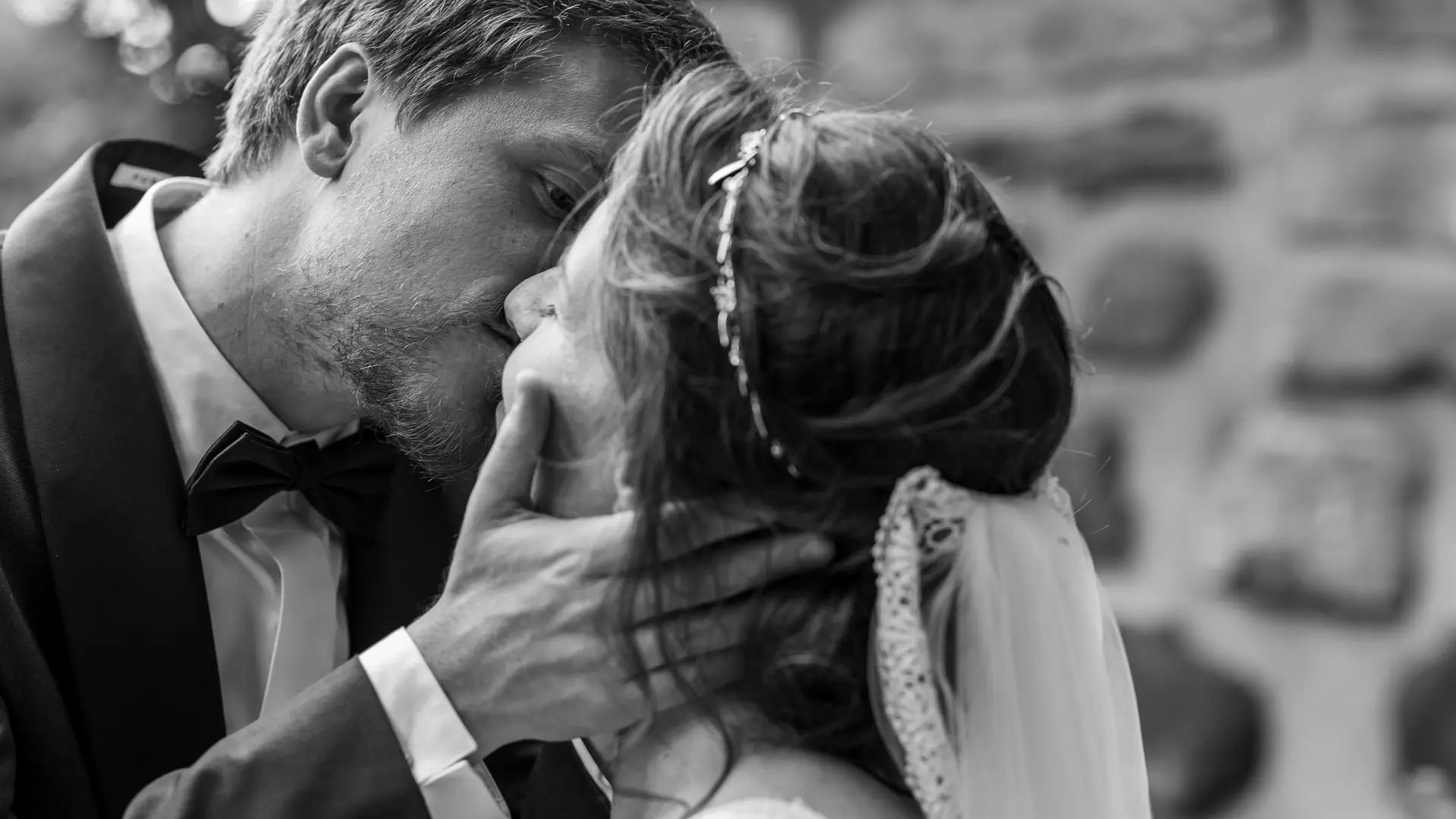 Gros plan en noir et blanc d'un couple de mariés s'embrassant. Le marié a une barbe et tient la tête de la mariée, qui porte un voile. La photo est axée sur l'émotion et la proximité des visages.